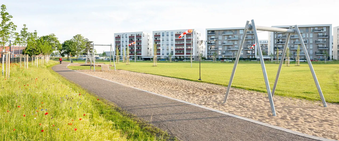 Neu angelegte Grünanlage in einem Kölner Neubaugebiet mit Weg, Wildblumenwiese und Spielgeräten