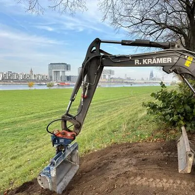 Bagger der R. Krämer GmbH bei Erdarbeiten mit der Kölner Skyline im Hintergrund