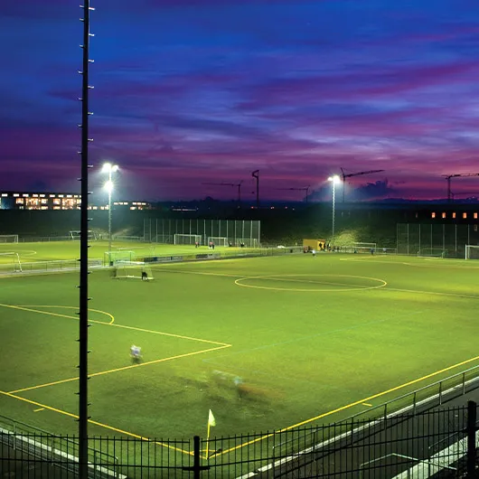 Fußballplatz mit Kunstrasen unter Flutlicht in der Abenddämmerung