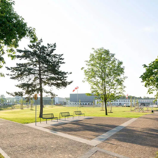 Öffentliche Parkanlage mit Bäumen, Sitzbänken und gepflastertem Platz