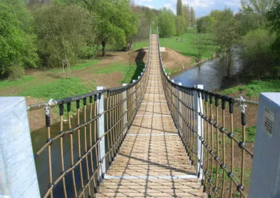 Hängebrücke über einen Wasserlauf in einer Grünanlage