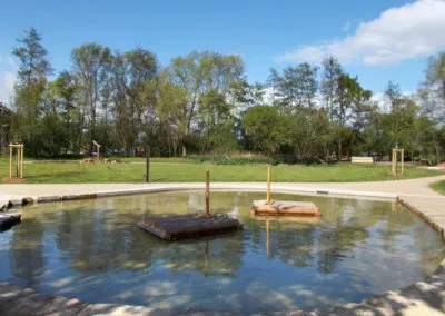 Wasserfläche mit Floß und begrünten Uferbereichen
