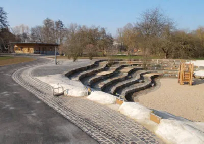 Wasserspielbereich mit gestuften Betonrinnen und Sandfläche